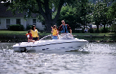 Mom, dad and kids on powerboat with house and trees in the background.